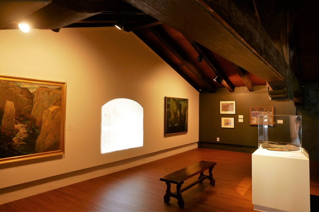 A gallery inside the Monterey Museum of Art, paintings hung under open wooden beams